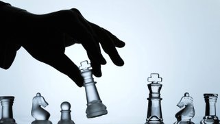 Artistic photo of a hand moving a chess piece on a chessboard.