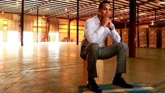 Photo of Ben Van Hook sitting on a small stool with his feet on a 3' by 3' wooden pallet.