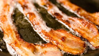 A picture of strips of bacon being fried.